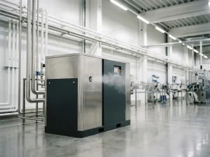 Ölfreier Industrie-Druckluftkompressor auf Fabrikboden mit Edelstahlrohren und sichtbarem Druckluftstrahl in moderner Produktionsanlage.